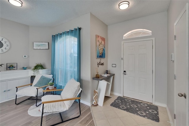 entrance foyer with baseboards, light wood finished floors, a healthy amount of sunlight, and a textured ceiling