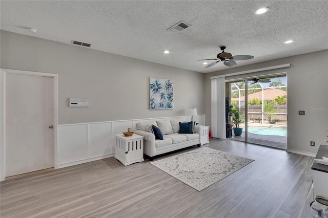 living room featuring light wood-style floors, visible vents, ceiling fan, and a textured ceiling