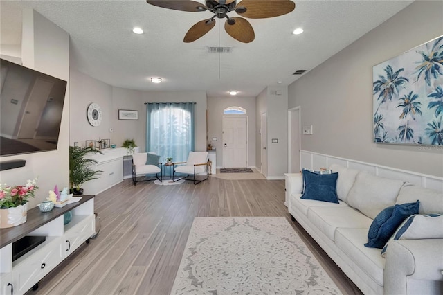 living room with light wood-style floors, visible vents, a ceiling fan, and a textured ceiling