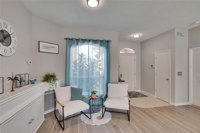 sitting room with a textured ceiling, visible vents, baseboards, and light wood-type flooring