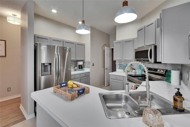 kitchen with light countertops, stainless steel appliances, pendant lighting, backsplash, and gray cabinetry