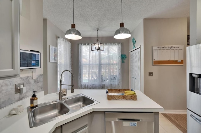 kitchen featuring stainless steel dishwasher, decorative light fixtures, a sink, a peninsula, and light countertops