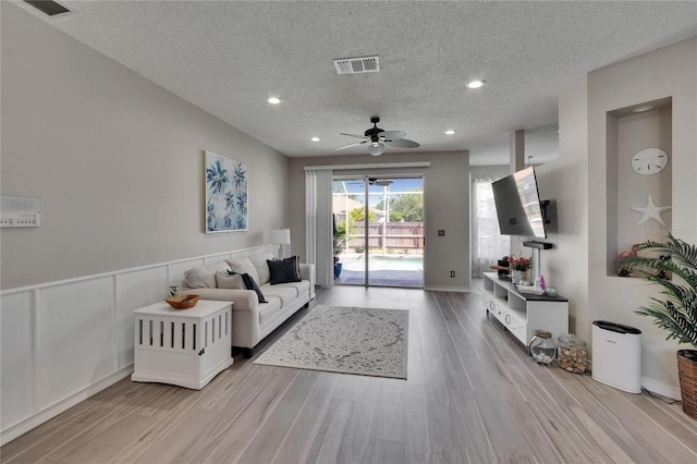 living room featuring a ceiling fan, light wood-style flooring, visible vents, and a textured ceiling
