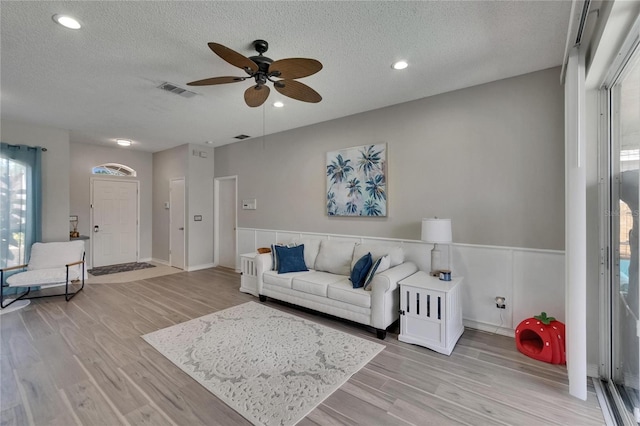 living room with a textured ceiling, light wood-style flooring, and ceiling fan