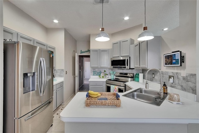 kitchen with a sink, a peninsula, backsplash, gray cabinetry, and appliances with stainless steel finishes