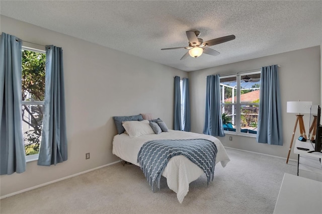 bedroom featuring light carpet, a textured ceiling, baseboards, and a ceiling fan