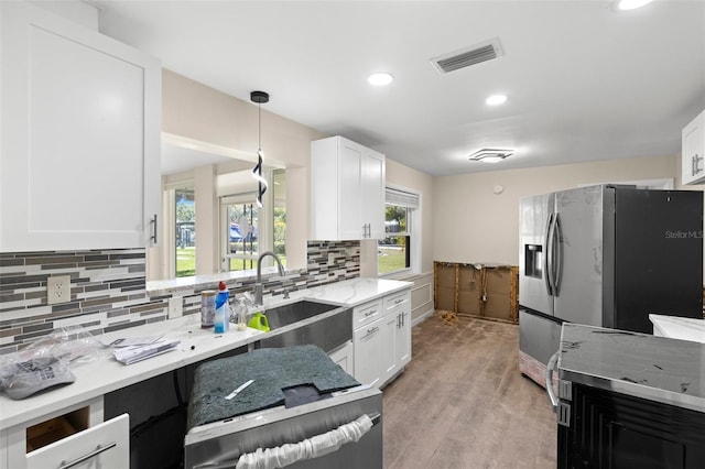 kitchen featuring light stone counters, white cabinetry, stainless steel refrigerator with ice dispenser, visible vents, and a sink