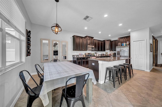 kitchen featuring dark brown cabinetry, baseboards, an island with sink, visible vents, and appliances with stainless steel finishes