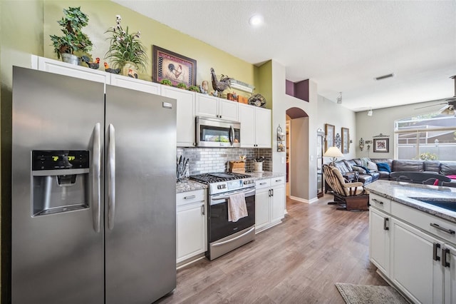 19750 Ellendale Dr, Land O Lakes, FL 34638 - kitchen featuring appliances with stainless steel finishes, arched walkways, open floor plan, white cabinets, and decorative backsplash