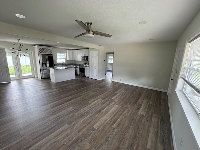 unfurnished living room with a textured ceiling, ceiling fan with notable chandelier, baseboards, and dark wood-style floors