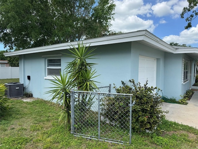 view of side of property featuring a yard, fence, central air condition unit, and stucco siding