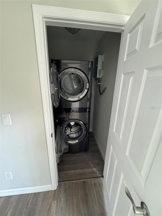laundry room with baseboards, wood finished floors, stacked washing maching and dryer, and laundry area