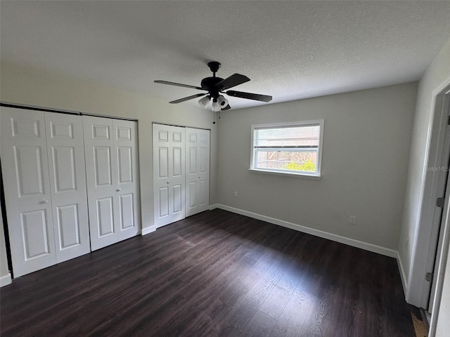 unfurnished bedroom featuring baseboards, dark wood-type flooring, a textured ceiling, and multiple closets