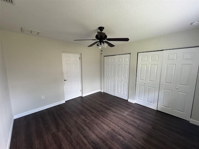 unfurnished bedroom with dark wood-type flooring, multiple closets, baseboards, and a textured ceiling