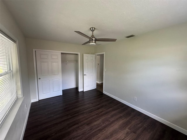 unfurnished bedroom featuring dark wood-type flooring, a closet, baseboards, and visible vents