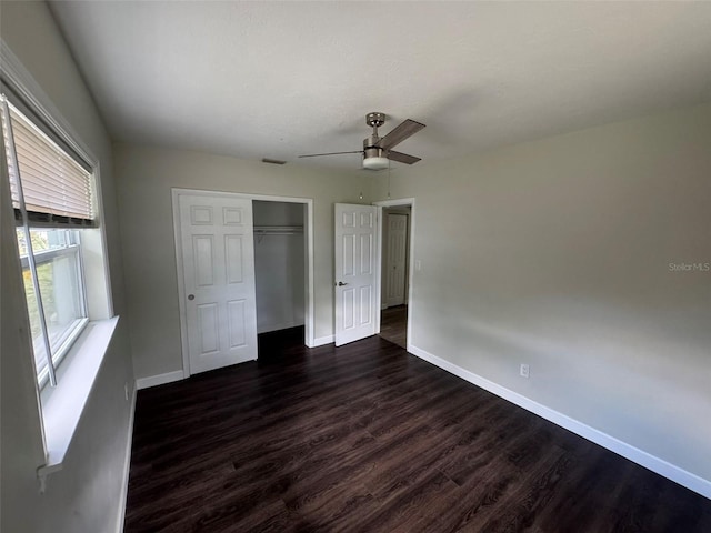 unfurnished bedroom with dark wood-style flooring, a closet, baseboards, visible vents, and ceiling fan