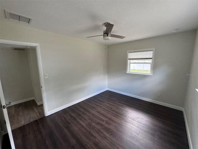 spare room with dark wood-style flooring, visible vents, ceiling fan, and baseboards