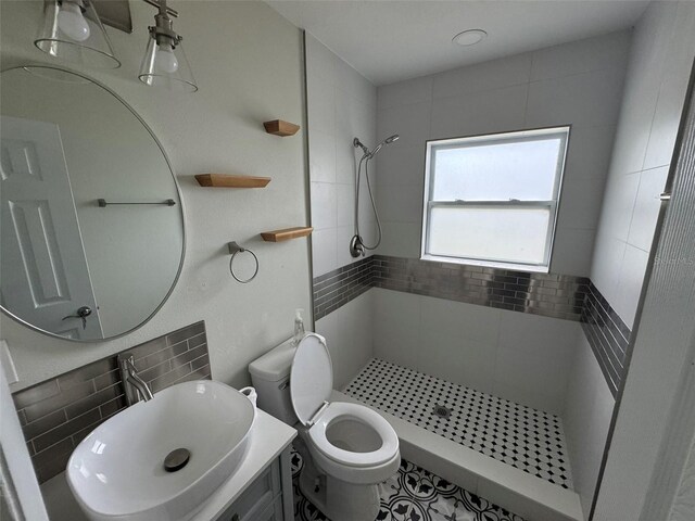 full bathroom with a tile shower, tasteful backsplash, vanity, and toilet