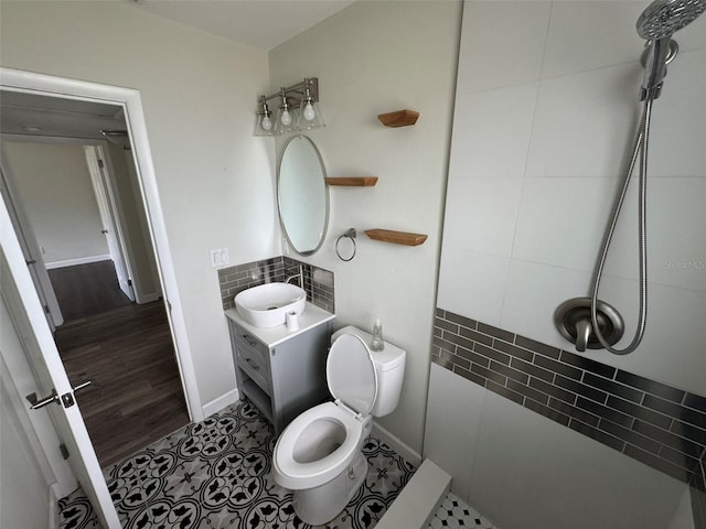 bathroom with baseboards, toilet, a tile shower, vanity, and backsplash