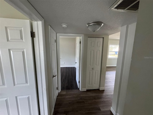corridor with visible vents, baseboards, a textured ceiling, and dark wood finished floors