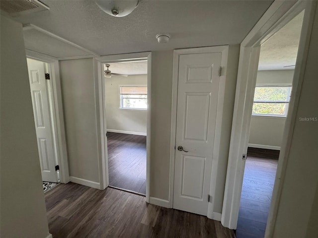 corridor with dark wood-type flooring, visible vents, a healthy amount of sunlight, and a textured ceiling