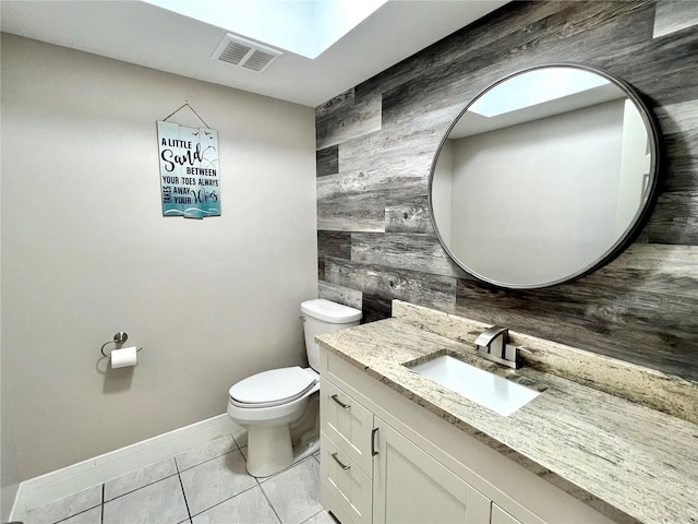 bathroom featuring visible vents, baseboards, wooden walls, toilet, and vanity