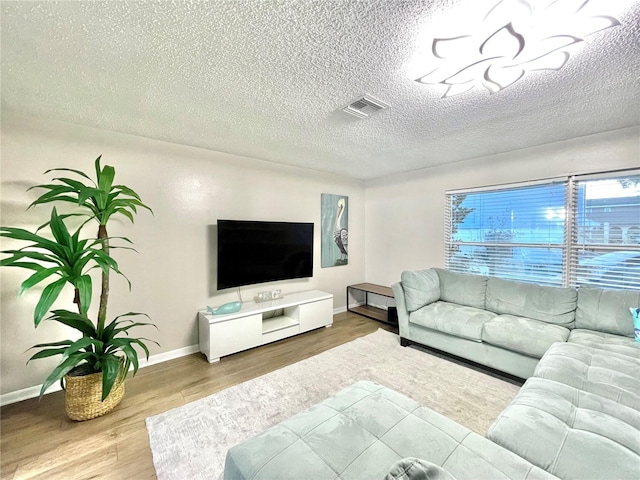 living room featuring wood finished floors, visible vents, a textured ceiling, and baseboards