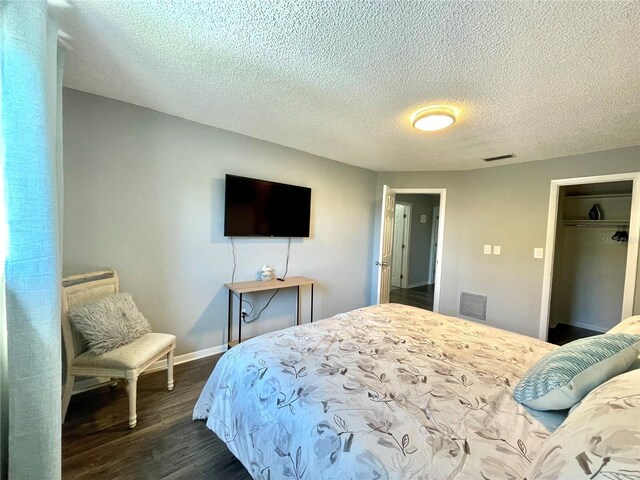 bedroom featuring a textured ceiling, visible vents, baseboards, and dark wood finished floors
