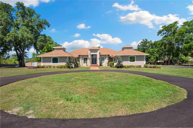 mediterranean / spanish-style house with a front lawn, stucco siding, and curved driveway