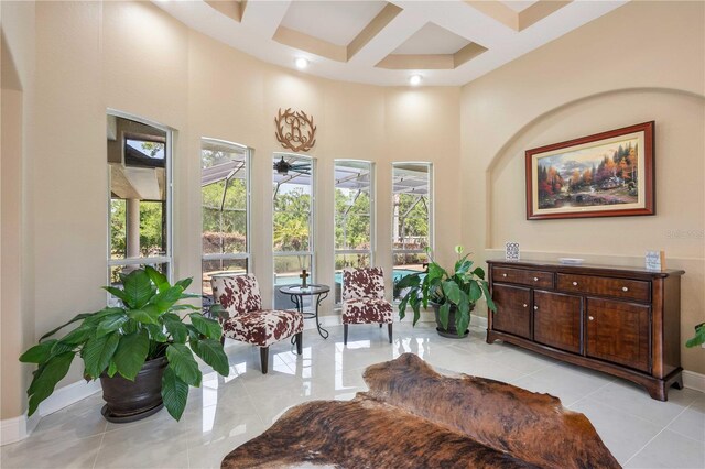sitting room featuring a ceiling fan, a towering ceiling, coffered ceiling, beamed ceiling, and baseboards