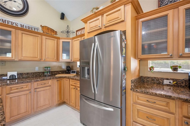 kitchen featuring dark stone counters, vaulted ceiling, stainless steel fridge, and light tile patterned floors