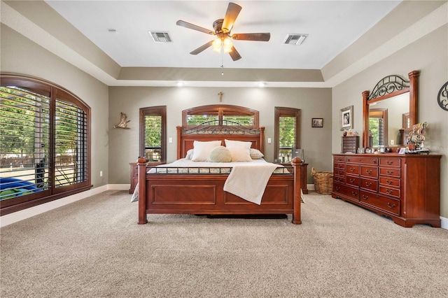 bedroom featuring visible vents, a raised ceiling, light colored carpet, and multiple windows