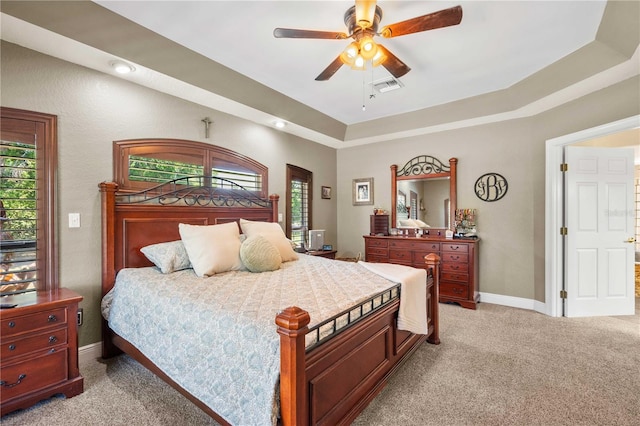 bedroom with light carpet, a raised ceiling, and multiple windows