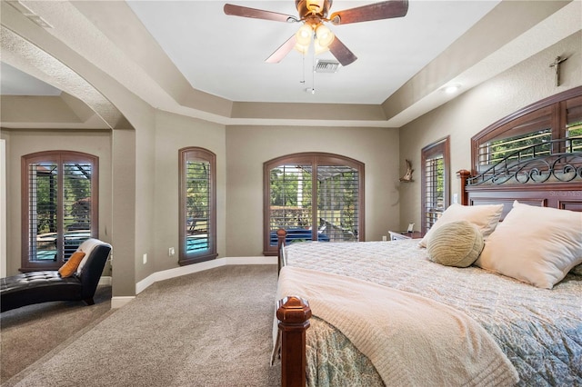carpeted bedroom with a tray ceiling, visible vents, a ceiling fan, and baseboards