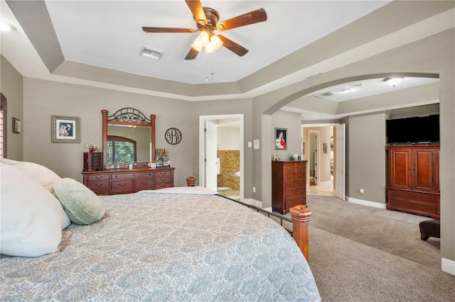carpeted bedroom featuring a tray ceiling, arched walkways, visible vents, baseboards, and a ceiling fan