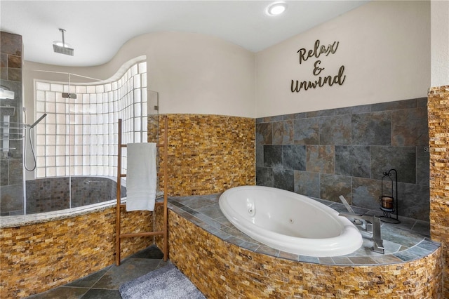 full bathroom featuring a jetted tub, stone finish flooring, tile walls, and a walk in shower