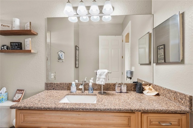 bathroom featuring a textured wall, toilet, and vanity