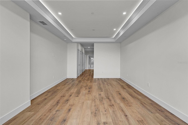 spare room with light wood-style flooring, visible vents, baseboards, a raised ceiling, and recessed lighting