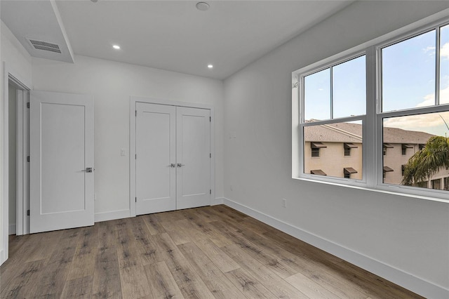 unfurnished bedroom with baseboards, multiple windows, visible vents, and wood finished floors
