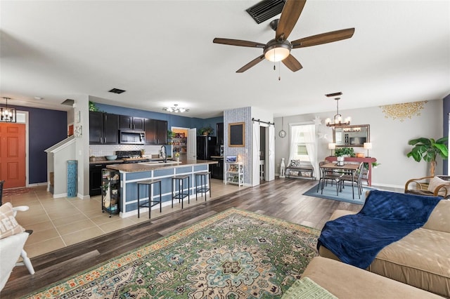 10101 Mangrove Well Rd, Ruskin, FL 33573 - living room featuring a barn door, visible vents, ceiling fan with notable chandelier, and light wood finished floors