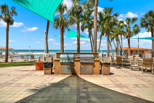 view of patio with area for grilling, fence, and a water view