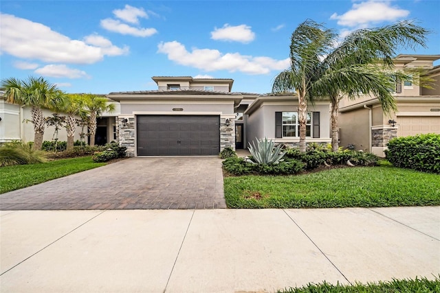 prairie-style house with an attached garage, stucco siding, stone siding, and decorative driveway