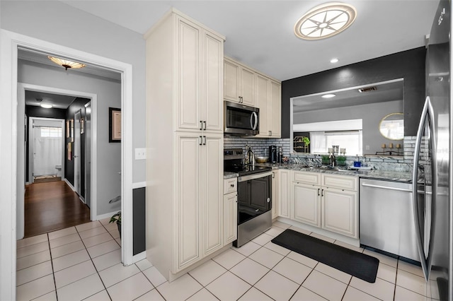 202 S Hesperides St, Tampa, FL 33609 - kitchen featuring appliances with stainless steel finishes, decorative backsplash, light tile patterned flooring, stone countertops, and cream cabinets
