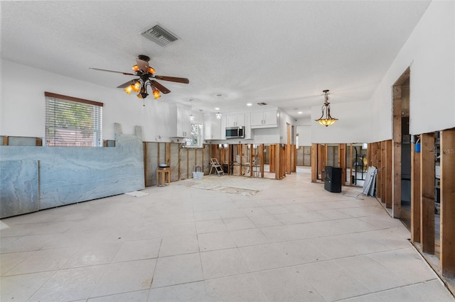 unfurnished living room with a textured ceiling, ceiling fan, and visible vents