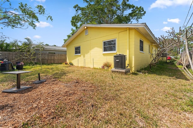 view of home's exterior with cooling unit, a fenced backyard, concrete block siding, and a lawn