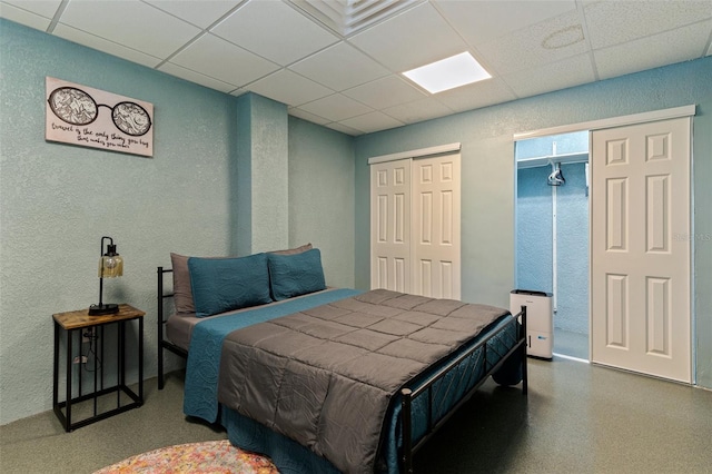 bedroom with multiple closets, a paneled ceiling, and a textured wall