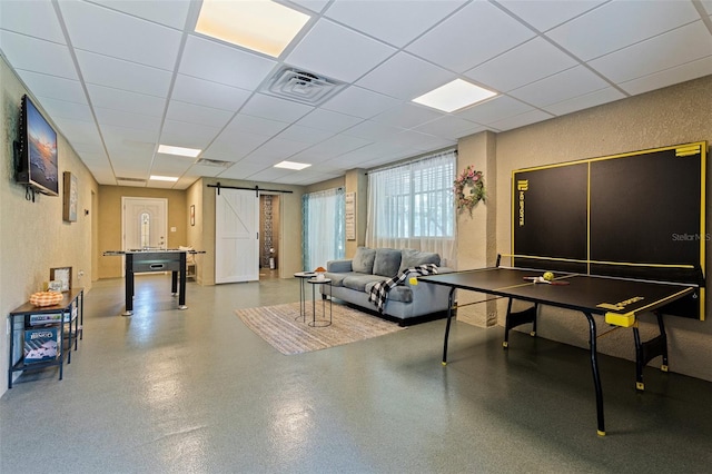 playroom with a textured wall, a barn door, visible vents, speckled floor, and a drop ceiling