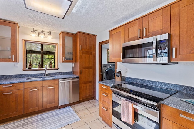 kitchen with washer / clothes dryer, a sink, appliances with stainless steel finishes, a textured ceiling, and brown cabinets