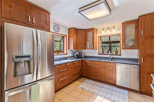 kitchen featuring light tile patterned floors, glass insert cabinets, a sink, stainless steel appliances, and brown cabinets