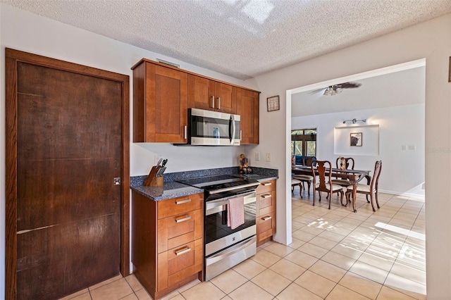 kitchen with light tile patterned floors, a textured ceiling, brown cabinets, ceiling fan, and stainless steel appliances